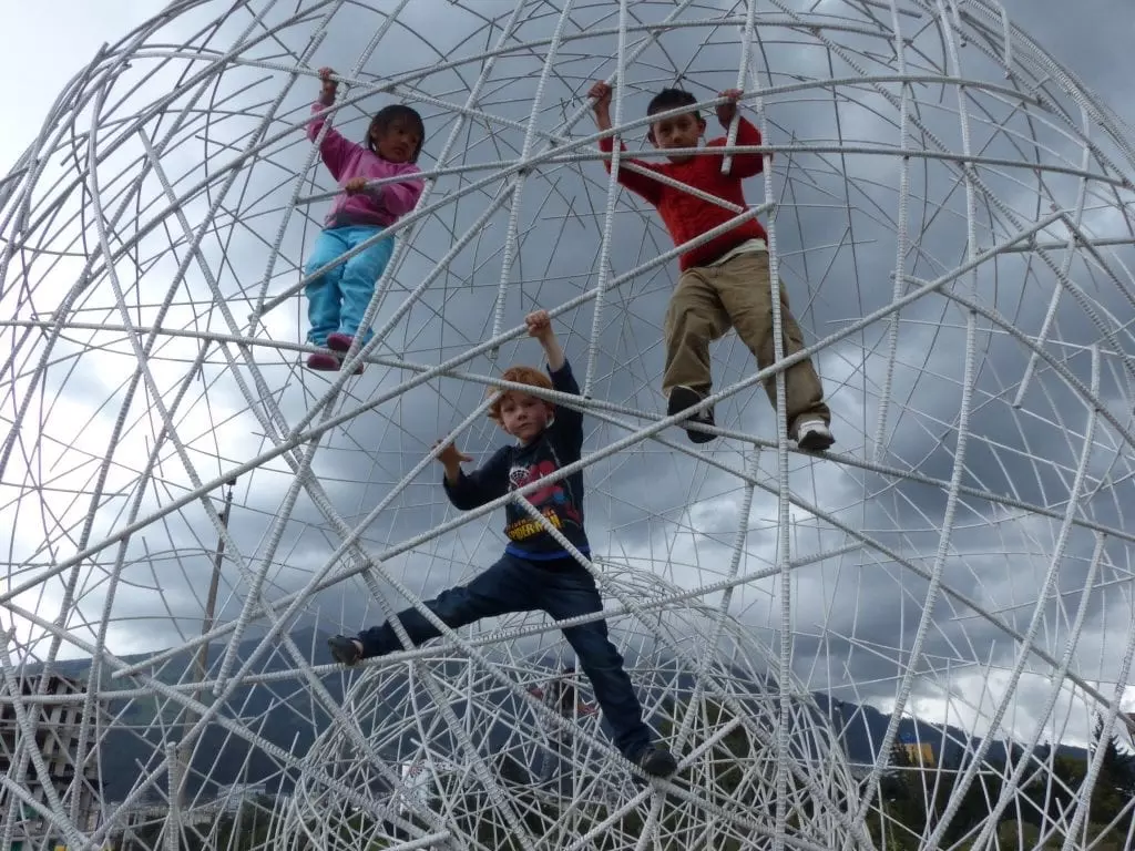 Kinder klettern in einem großen weißen, kugelförmigen Klettergerüst vor grauem