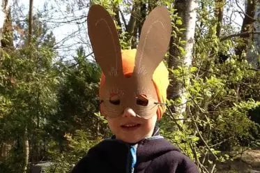 Kind mit selbst gebastelter Osterhasen-Maske im Grünen