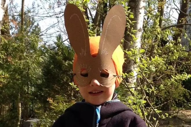 Kind mit selbst gebastelter Osterhasen-Maske im Grünen