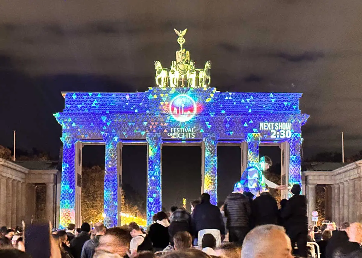 Nachts versammelte sich eine Menschenmenge vor dem Berliner Brandenburger Tor, das während des Festival of Lights mit Kindern mit bunten Lichtern und digitalen Projektionen beleuchtet wird.