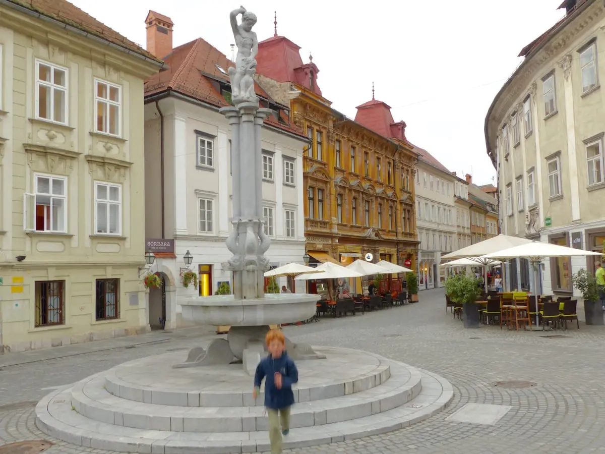 Slowenien Urlaub mit Kind Charmante historische Gebäude im Herzen der Altstadt von Ljubljana gruppieren sich um einen autofreien Platz mit einem Brunnen, der ein Kind im Slowenien Urlaub zum Spielen und Rennen einlädt.