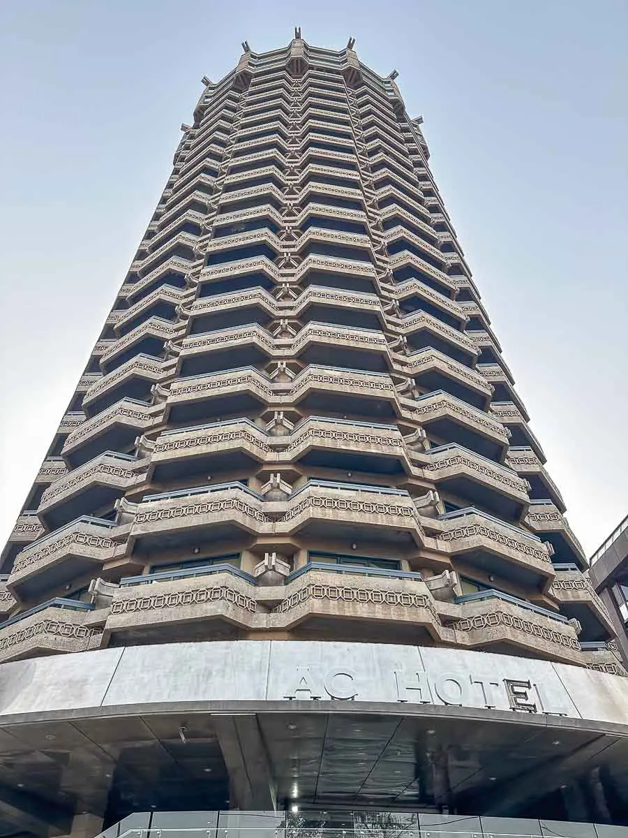 Ein hohes, mehrstöckiges Gebäude mit markanten, geometrisch geformten Balkonen, von unten gesehen; auf dem Schild am Eingang steht „AC HOTEL“. Vor dem Hintergrund eines klaren Himmels ist dieses moderne Bauwerk eine der bemerkenswerten Sehenswürdigkeiten in Las Palmas de Gran Canaria.