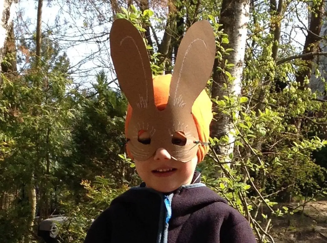 Kind mit selbst gebastelter Osterhasen-Maske im Grünen