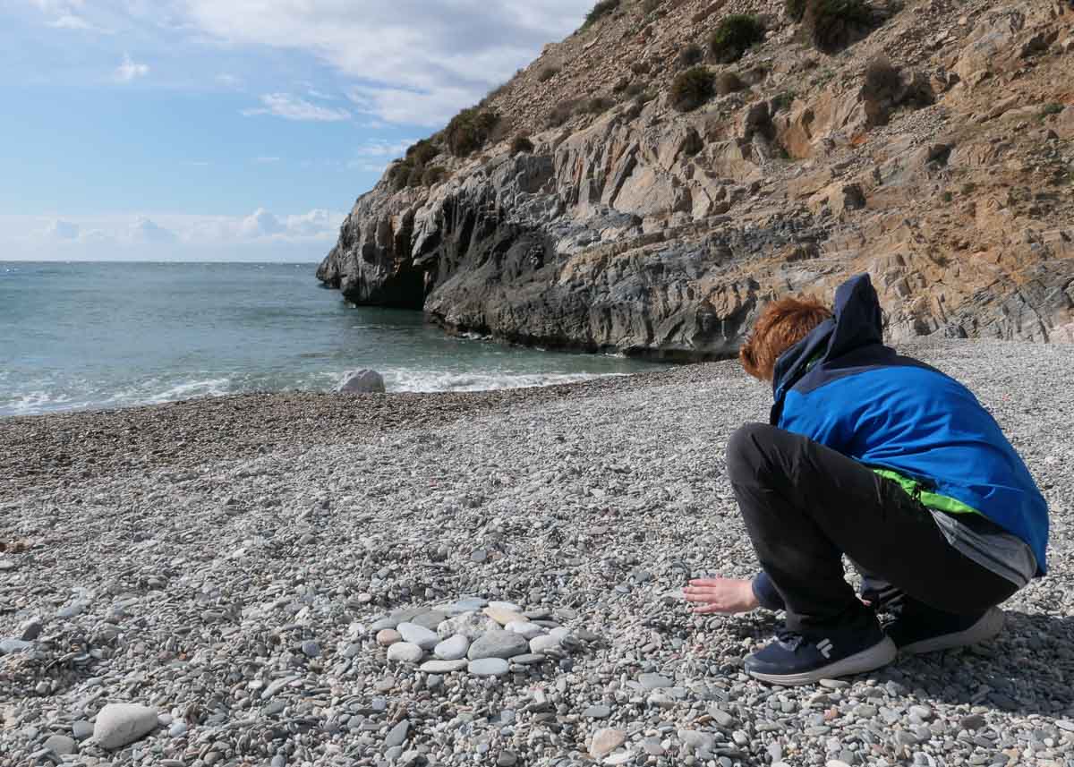 Kind spielt am Strand mit Kieseln beim Roadtrip durch Andalusien