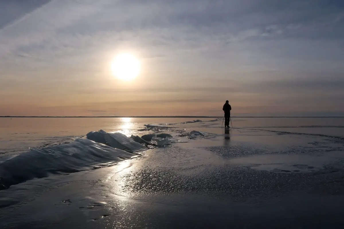 flachstehende Wintersonne über einem zugefrorenen See in Schweden mit Spaziergänger