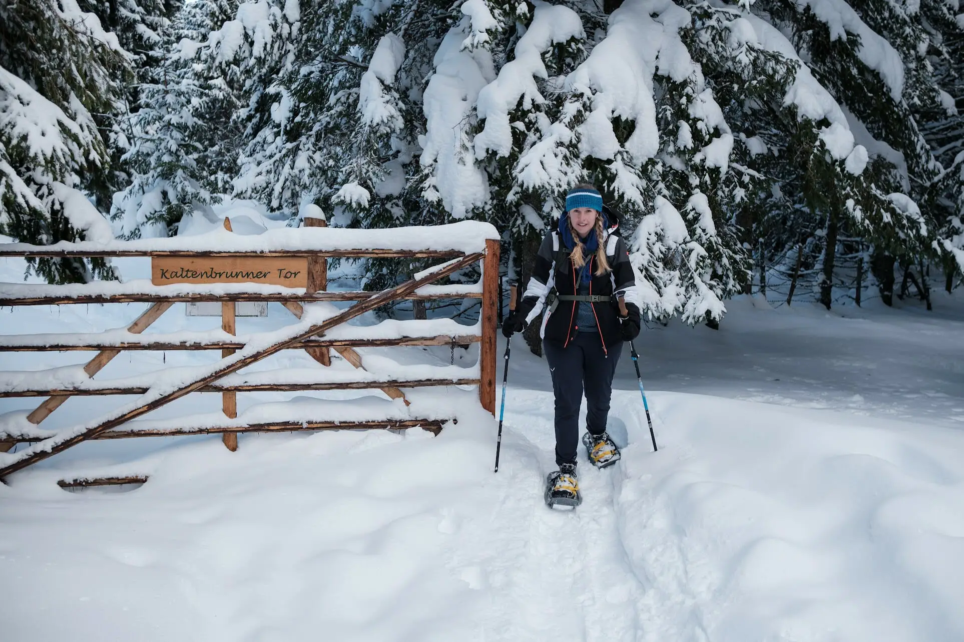 Frau mit Schneeschuhen an einem Gattertor im verschneiten Winterwald