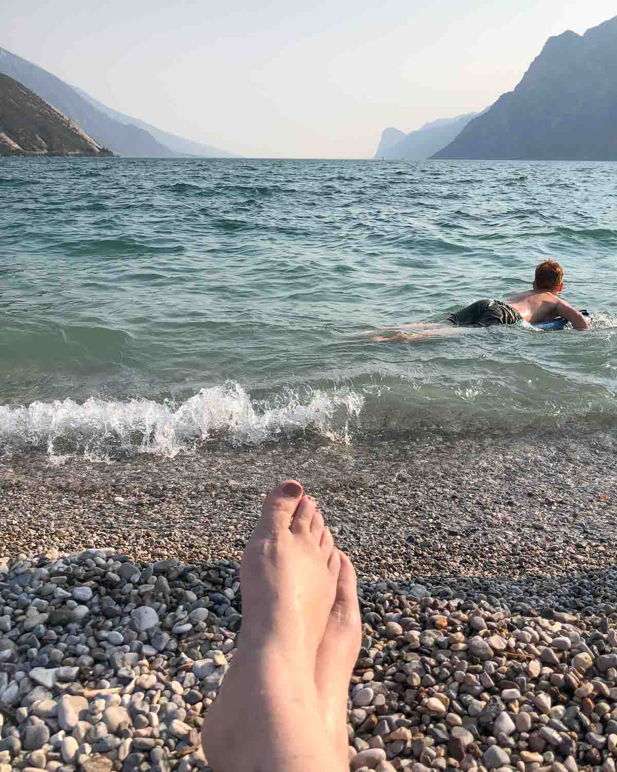 Kieselstrand am Gardasee mit planschendem Kind und entspannten Frauenfüßen