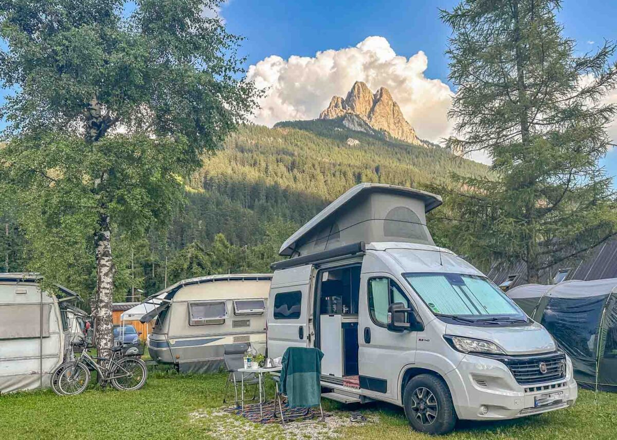 Camper mit Aufstelldach auf Campingplatz im Fassatal mit Dolomitengipfeln im Hintergrund