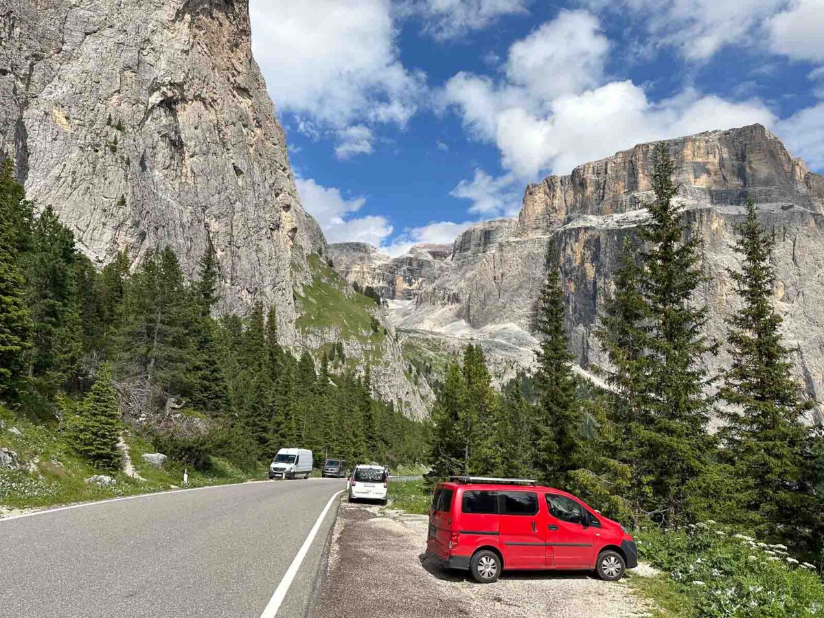 Straße vom Sellajoch ins Fassatal mit geparktem rotem Auto und hohen Felsgipfeln