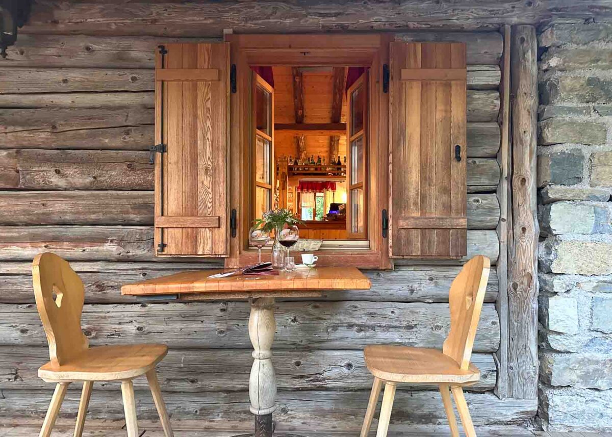 Traditioneller Holztisch und Stühle vor einer Almhütte mit Fensterläden 