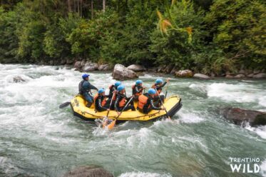 Gelbes Schlauchboot mit 6 Leuten und 1 Guide bei einer Rafting Tour auf dem Wildwasser Fluss Noce im Trentino vor einer Stromschnelle