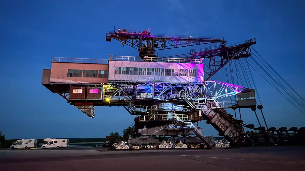 Die gigantische Bergbaumaschine Mad Max in Ferropolis bei Nacht mit Beleuchtung. Darunter stehen Wohnmobile 