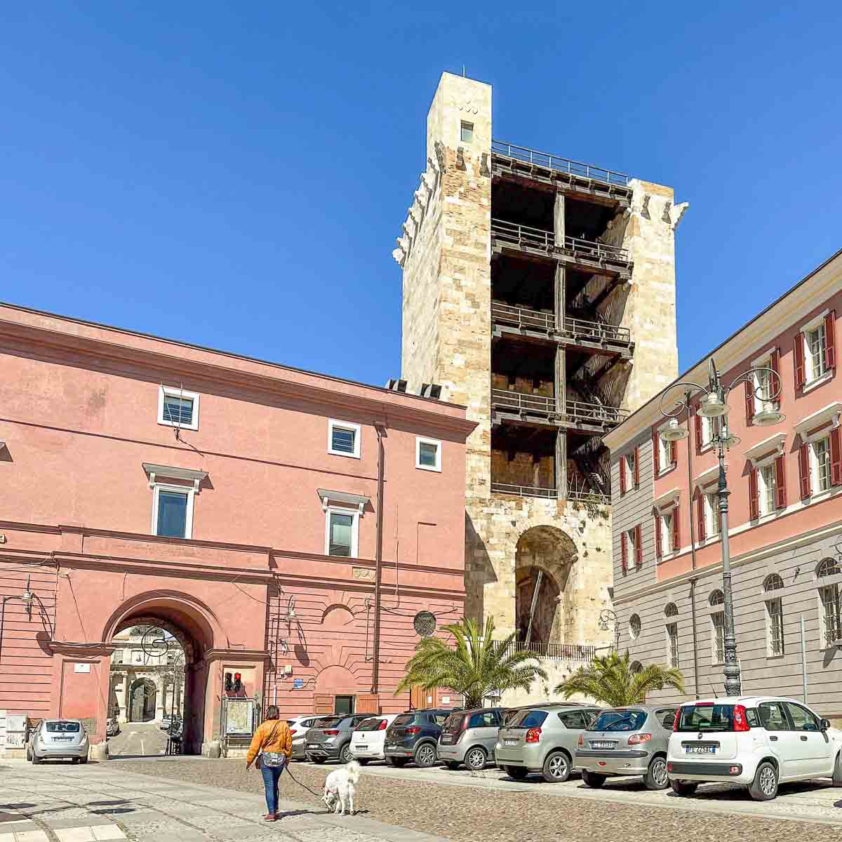 In Cagliari Altstadt stehen viele einzigartige historische Wehrtürme, wie der Torre di San Pancrazio , der zwischen klassizistischen Gebäuden hinter einem Platz aufragt, auf dem eine Frau bummelt.