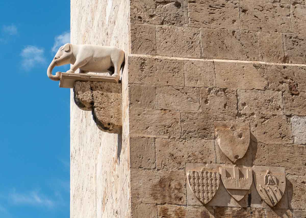 Wappen und eine Elefantenfigur auf einem Podest an einem alten Sandsteinturm