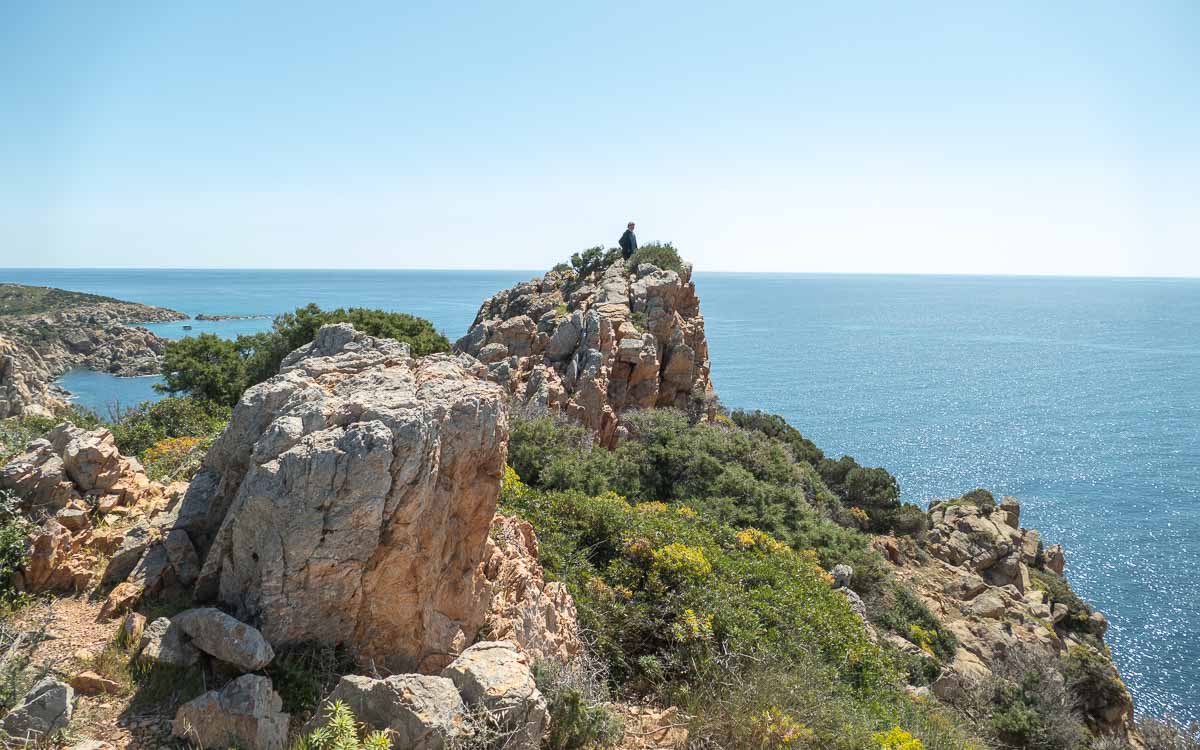 Ein Wanderer steht auf einer Felsnase über der Südküste von Sardinien.