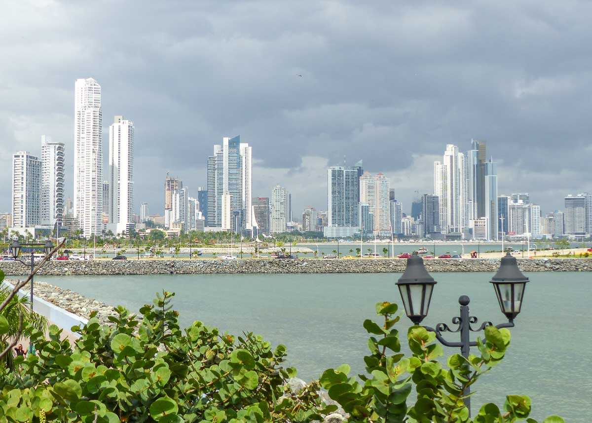 Skyline von Panama City über das Meer hinweg mit tropischen Bäumen und hübschen historischen Straßenlaternen im Vordergrund