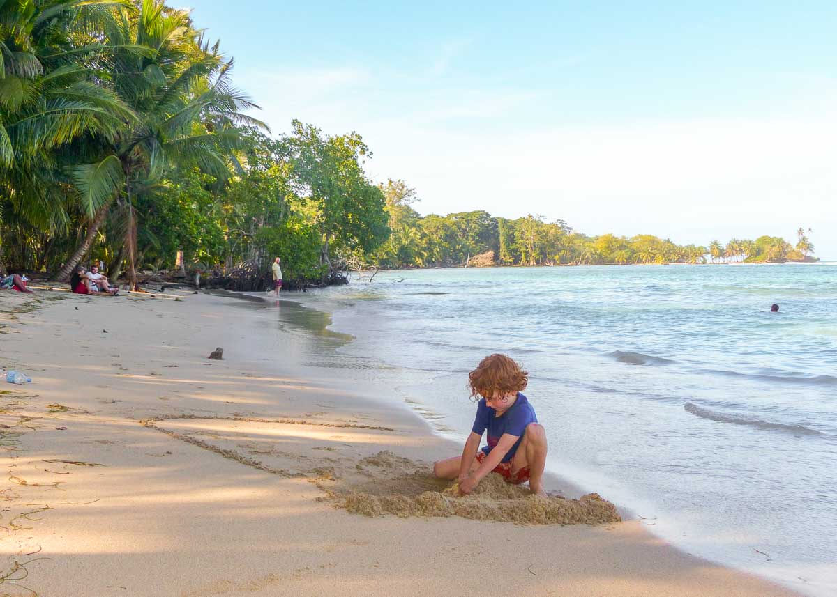 Ein kleines Kind spielt im Sand an einem Strand mit Palmen und Sand in Panamas karibischen Inselparadies Bocas del Toro.