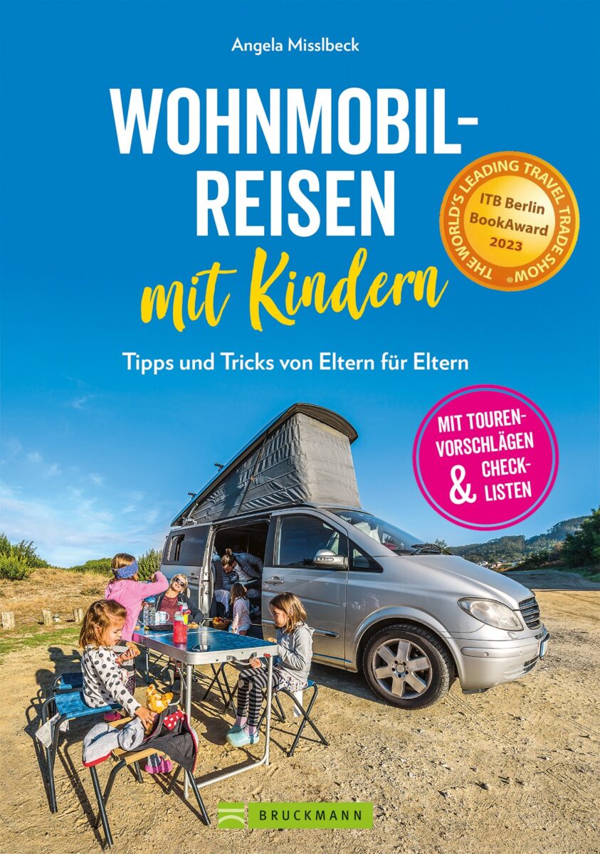 wohnmobilreisen-mit-kindern Eine Familie mit zwei Kindern sitzt an einem Tisch vor einem grauen Wohnmobil, isst und genießt die Natur. Der Text auf dem Einband lautet: „Wohnmobilreisen mit Kindern – Tipps und Tricks von Eltern für Eltern.“.
