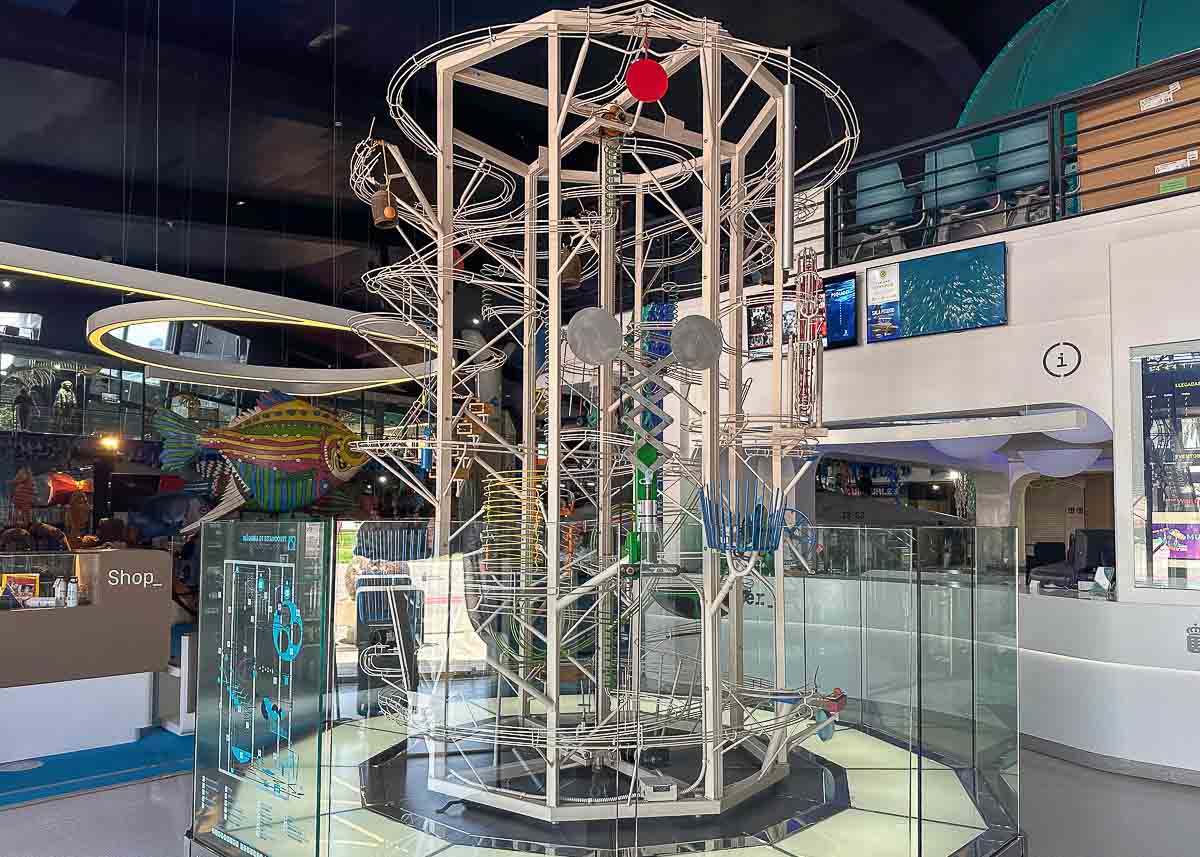 Eine große Metall-Kugelbahn mit Schienen, Hebeln und bunten Kugeln ist in einem modernen Innenraum mit Glaswänden, Beschilderungen und einem Zwischengeschoss darüber ausgestellt – das Museo Elder ist perfekt für Las Palmas mit Kindern.